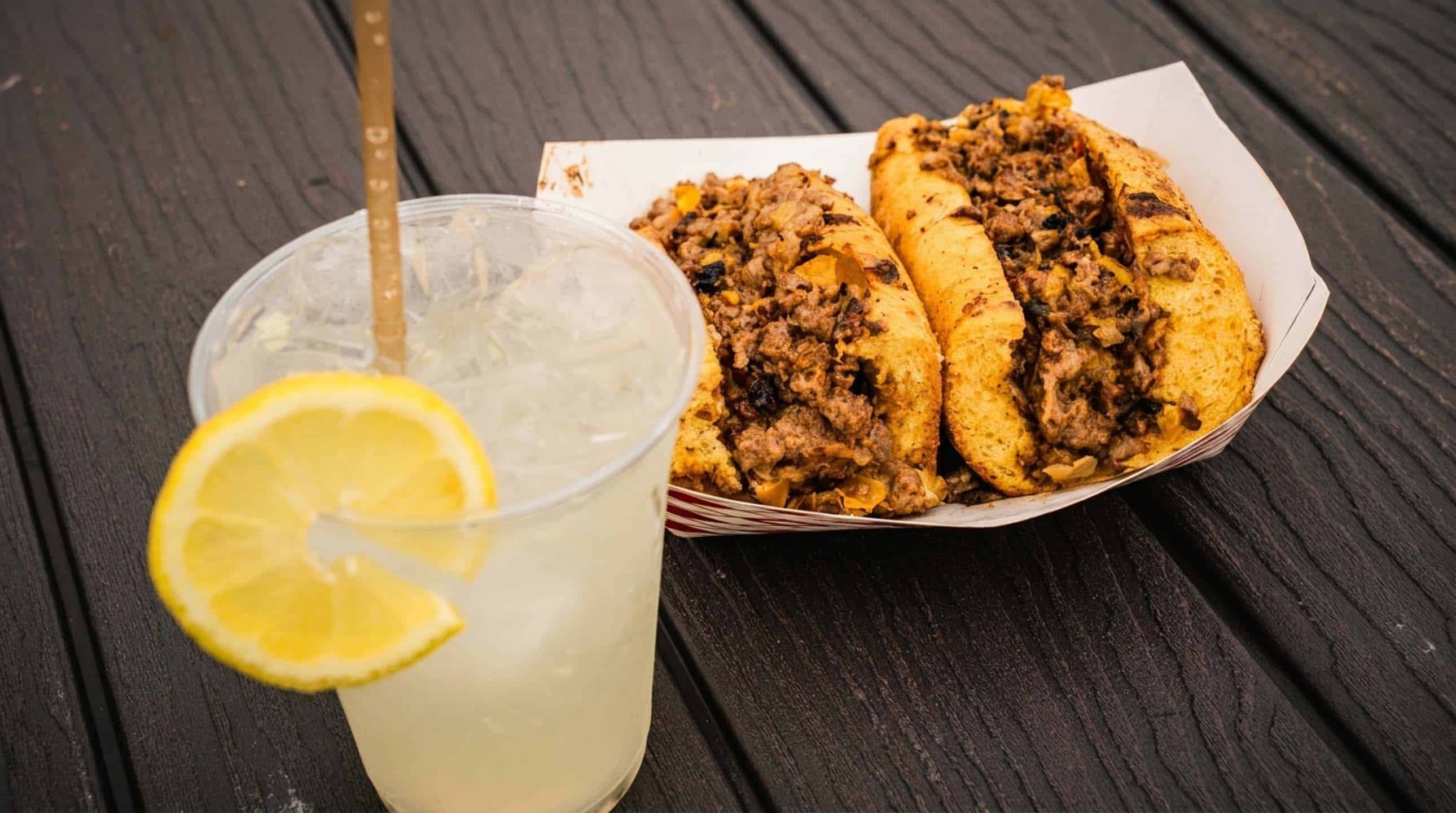 A cup of fresh-squeezed lemonade with a lemon wheel next to a cheesesteak