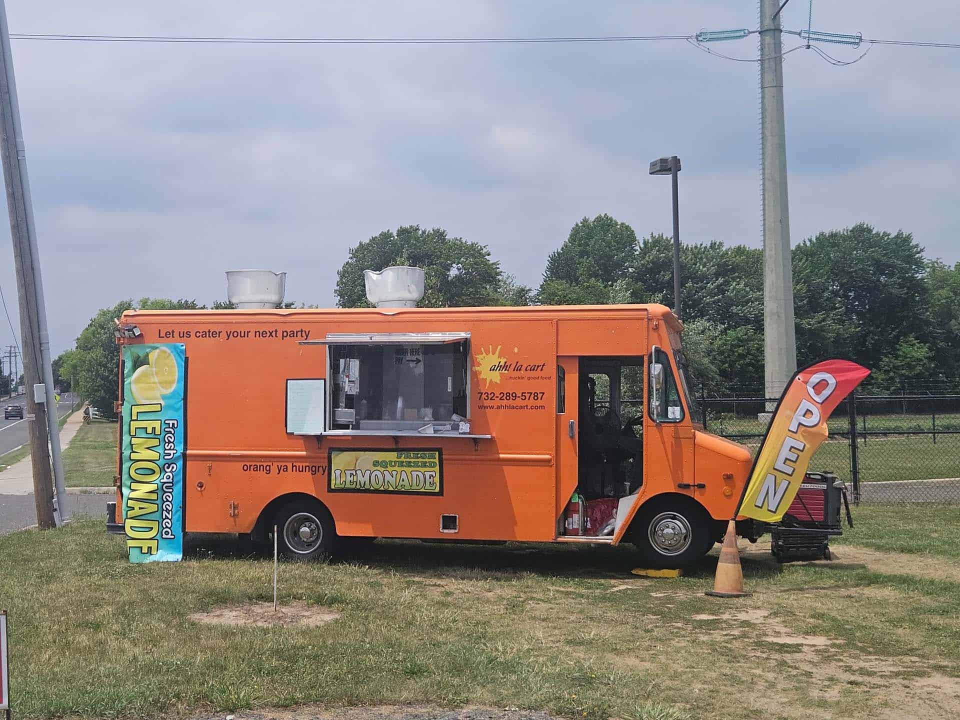 The bright orange Ahh la Cart food truck parked on the grass with its fresh-squeezed lemonade flag flying